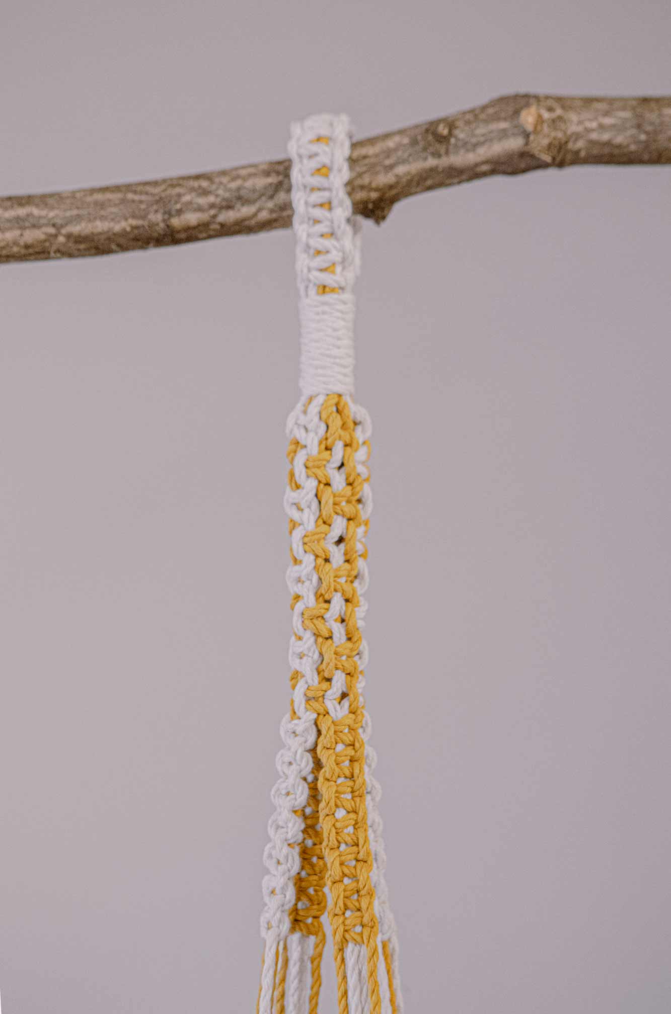 Detalle del agarre de un macetero artesanal de macramé hecho de algodón ecológico en color crudo y mostaza
